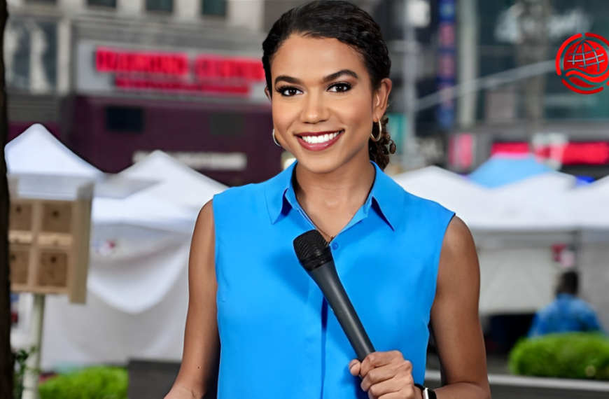 A smiling woman in a blue sleeveless blouse holds a microphone, standing outdoors with white tents in the background and blurred street signs. A red globe logo appears in the top right corner.