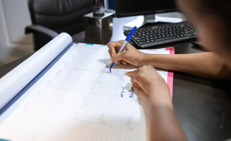 Person planning their schedule on a desk calendar using AI tools