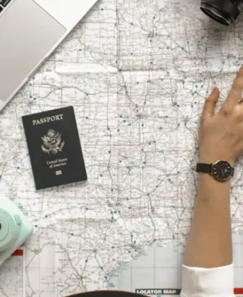 Hand pointing at a map with laptop and passport, planning a trip with AI