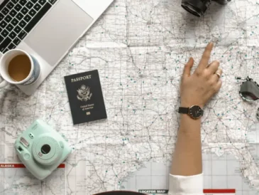 Hand pointing at a map with laptop and passport, planning a trip with AI
