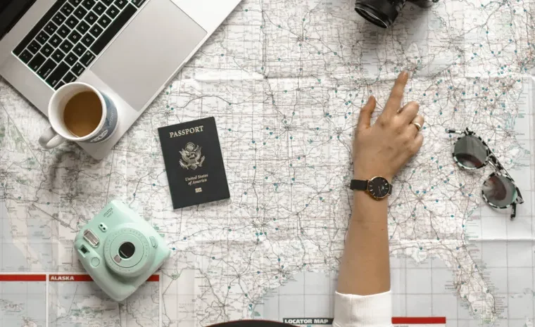 Hand pointing at a map with laptop and passport, planning a trip with AI