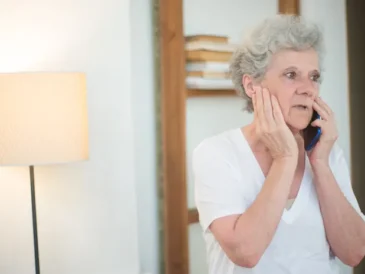 Elderly woman looking concerned while taking a phone call at home
