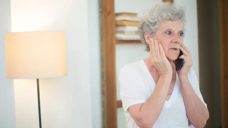 Elderly woman looking concerned while taking a phone call at home
