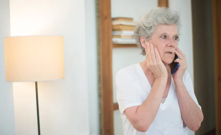 Elderly woman looking concerned while taking a phone call at home